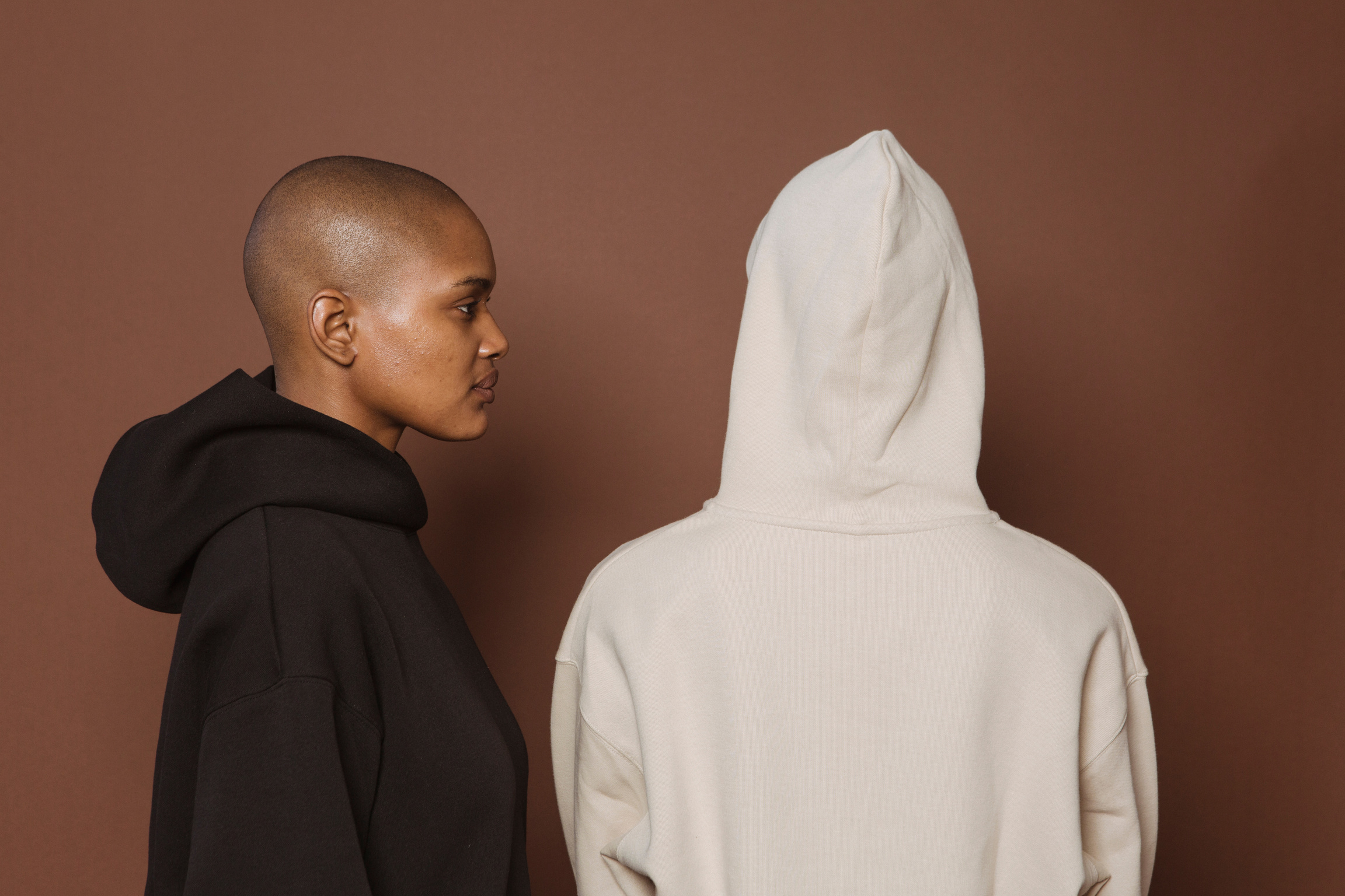 Black bald woman in hoodie near person in studio